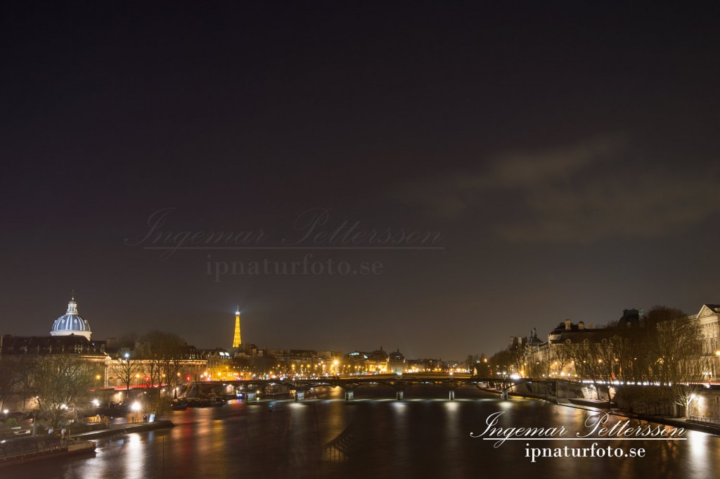 Sakta rinner Seine fram genom vackra Paris en sen natt. och Eiffeltornet skickar sitt sken genom natten.